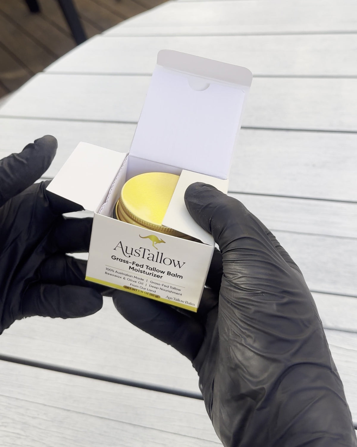 Gloved hands holding the AusTallow printed box with the gold-lidded tallow balm jar inside